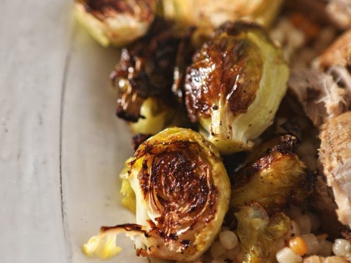 Close up of roasted brussels sprouts on a white serving tray with meat and couscous