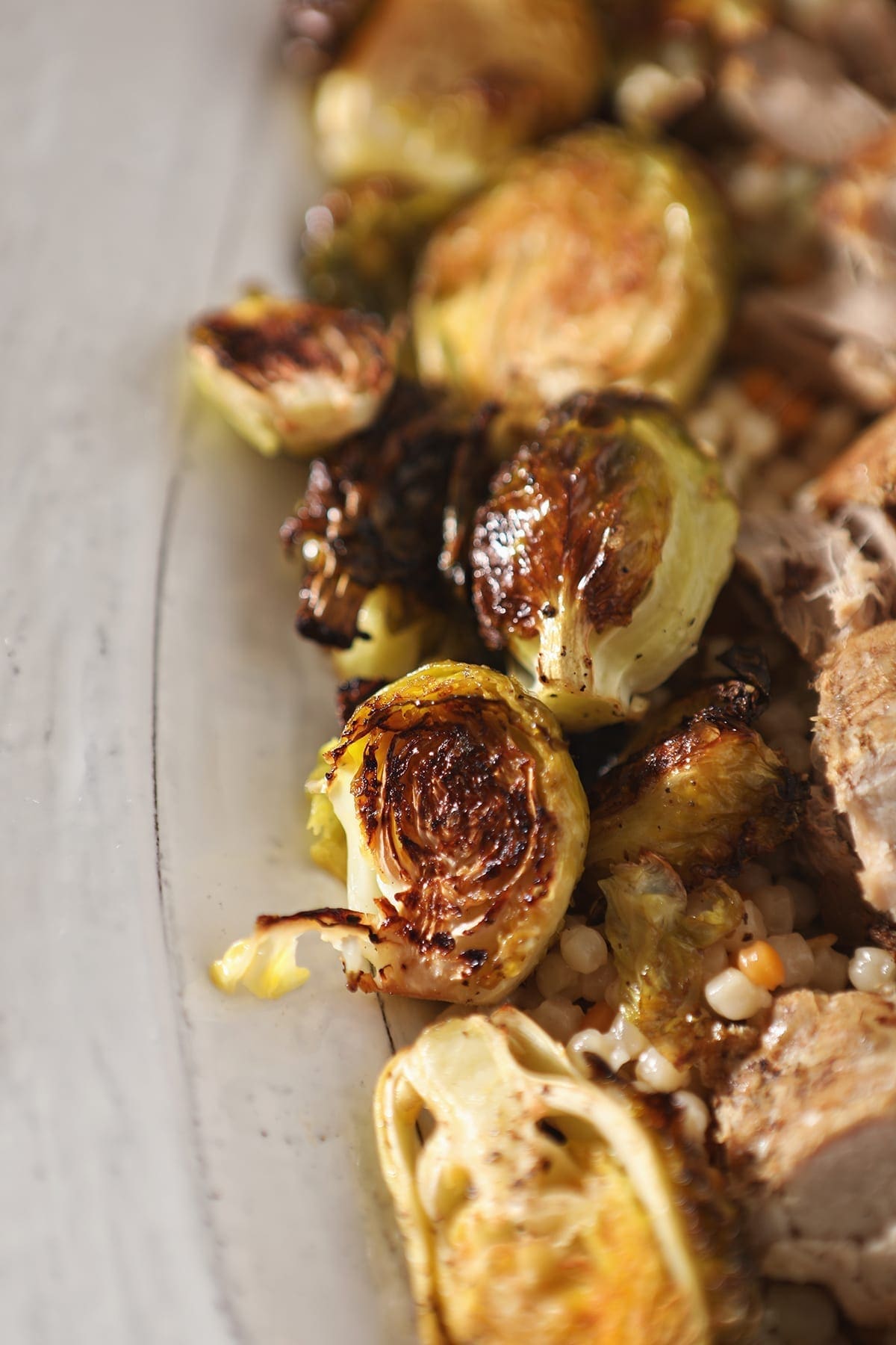 Close up of roasted brussels sprouts on a white serving tray with meat and couscous