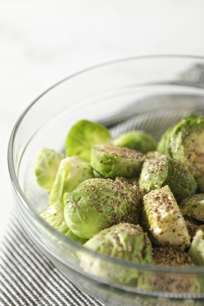 Close up of halved brussels sprouts in a bowl seasoned with salt and pepper