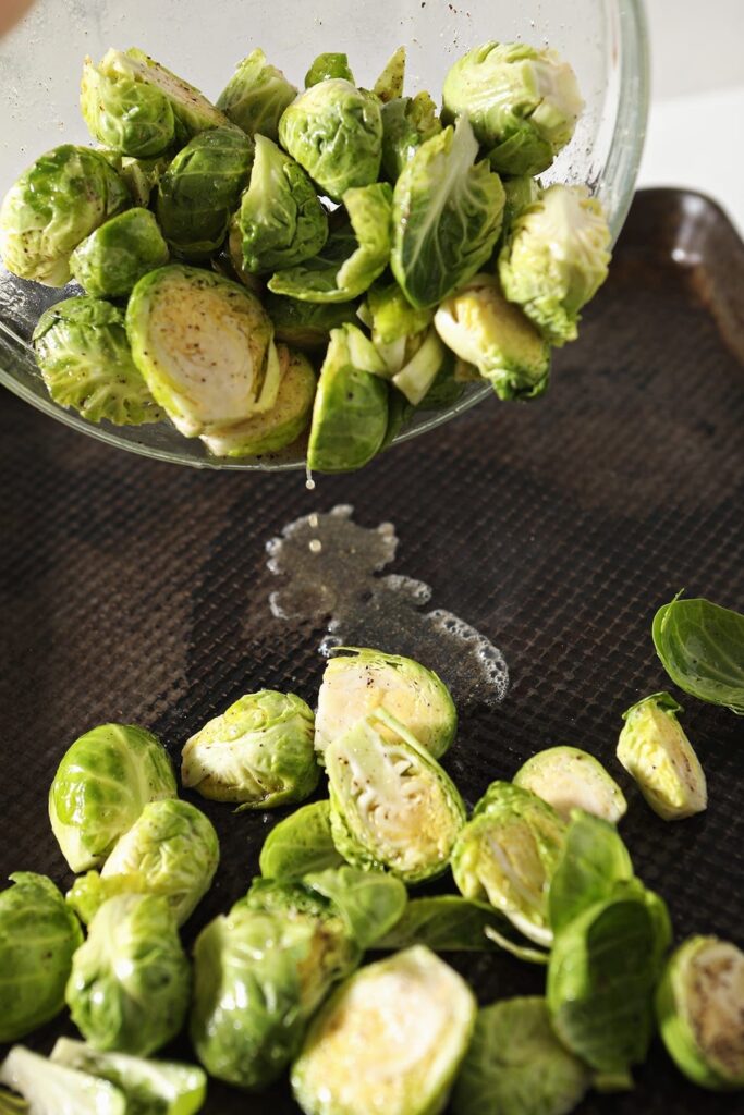 Halved brussels sprouts are dropped onto a hot baking sheet