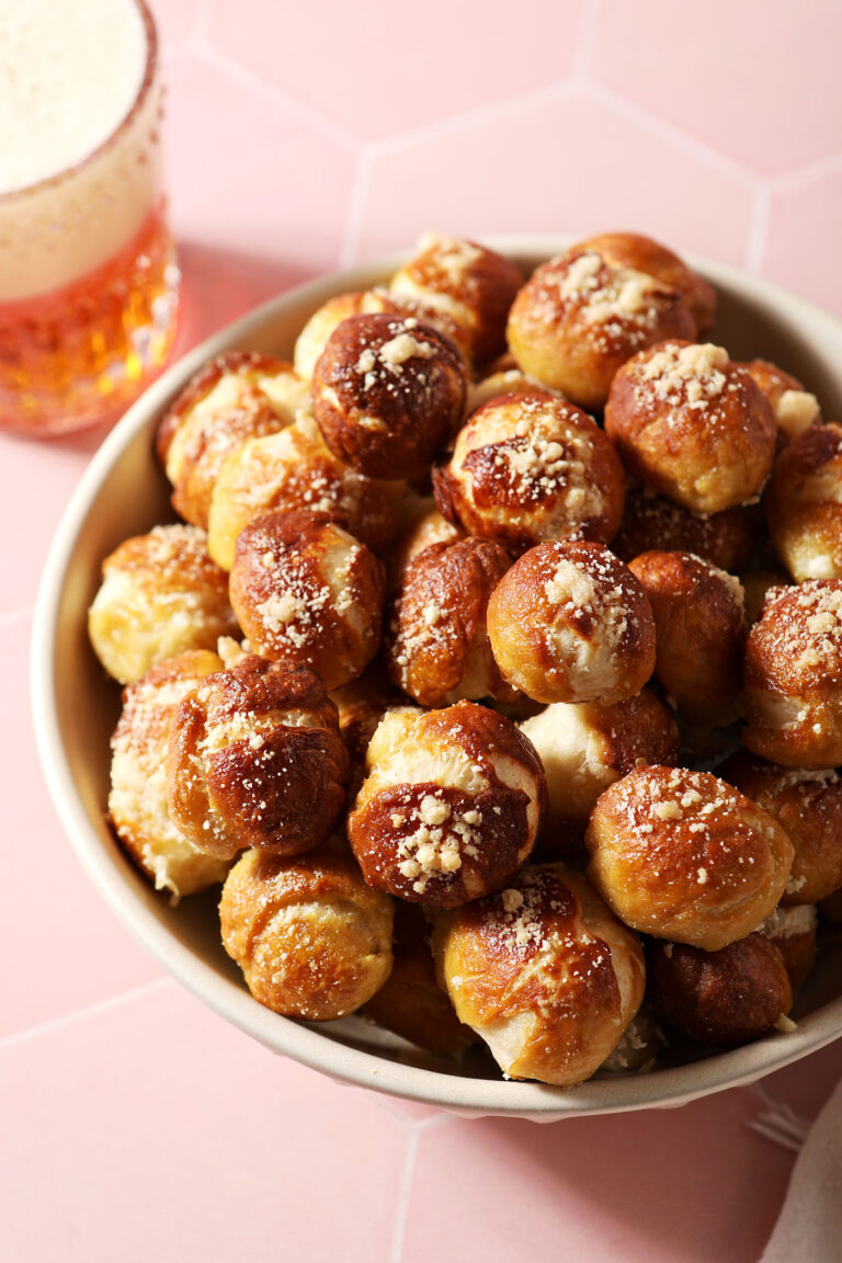 Close up of a bowl holding soft Parmesan Pretzel Bites next to a mug of beer on a pink tiled surface