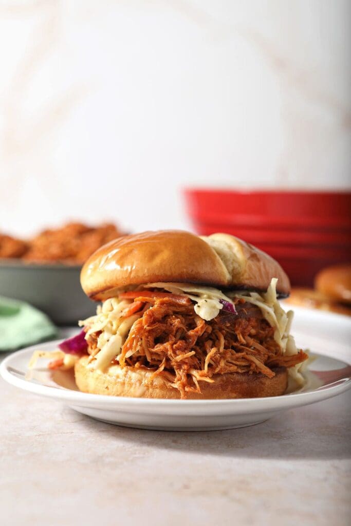 A BBQ chicken sandwich with slaw on a white plate