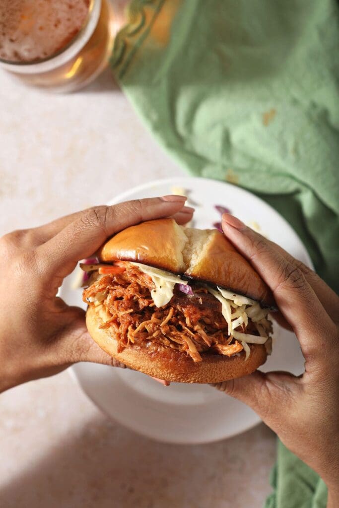 A woman holds a BBQ chicken sandwich above a plate