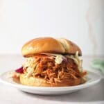 A BBQ chicken sandwich on a plate topped with coleslaw