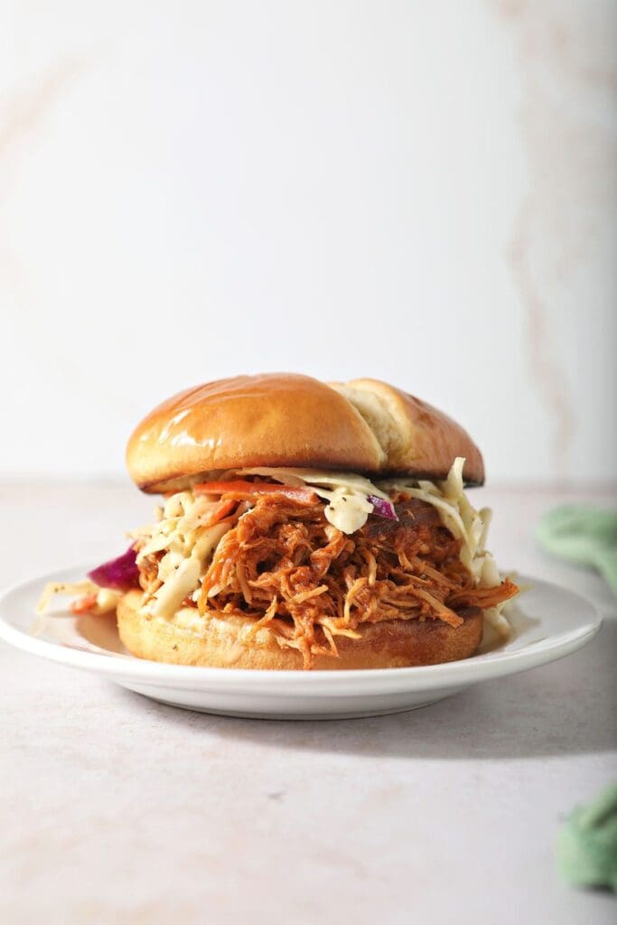 A BBQ chicken sandwich on a plate topped with coleslaw