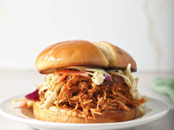 A BBQ chicken sandwich on a plate topped with coleslaw