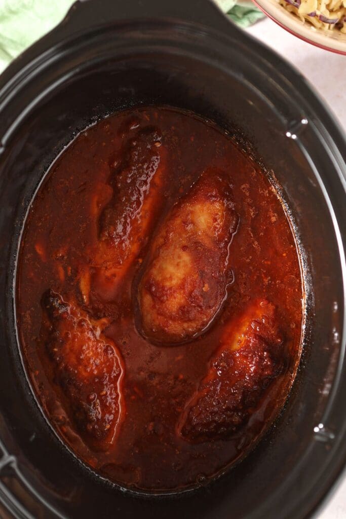 Cooked chicken breasts in BBQ sauce ingredients to make slow cooker BBQ chicken sandwiches after cooking