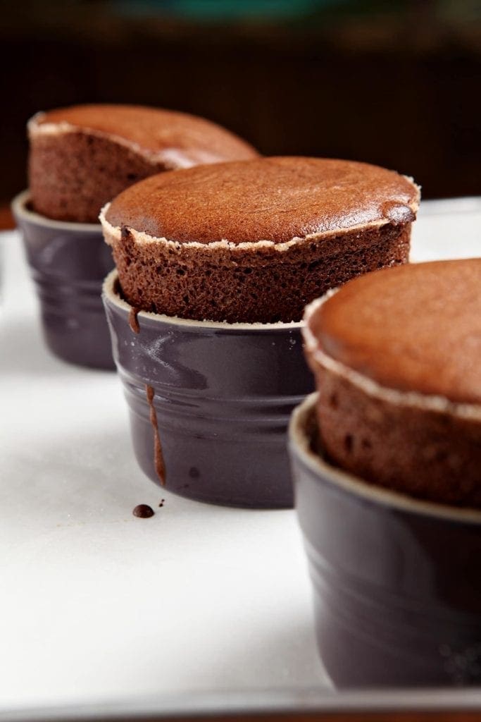 Three Dark Chocolate Soufflés sit on a baking sheet, straight out of the oven