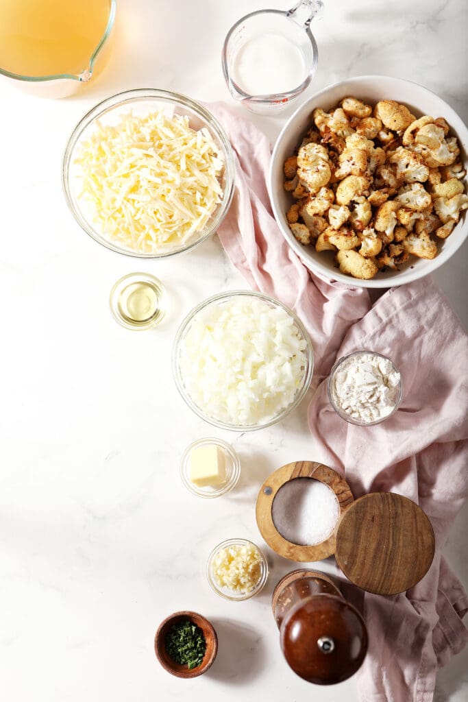 Ingredients to make roasted cauliflower soup in bowls on marble with a pink linen