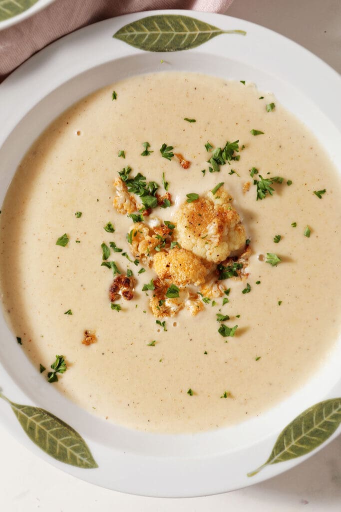 Close up of a bowl of roasted cauliflower cheese soup from above garnished with cauliflower and chopped parsley