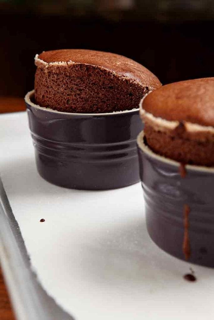 Two risen chocolate souffles on a baking sheet