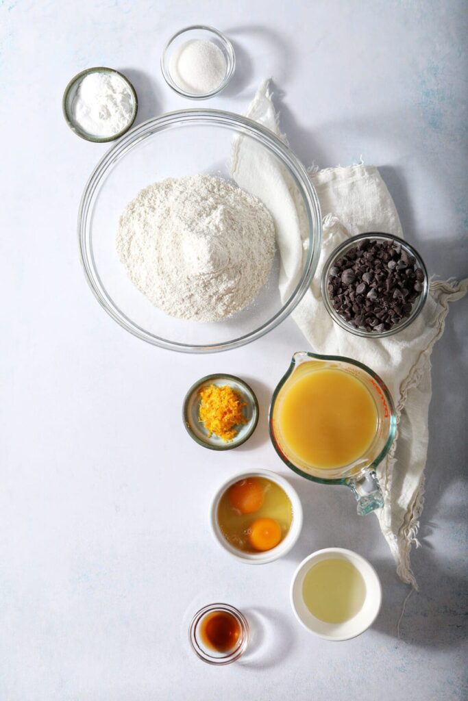 Ingredients to make Orange Pancakes with Chocolate Chips in bowls on a marble surface