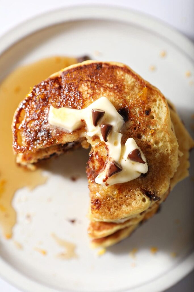 A sliced-into stack of orange pancakes with syrup, butter and mini chocolate chips as garnish