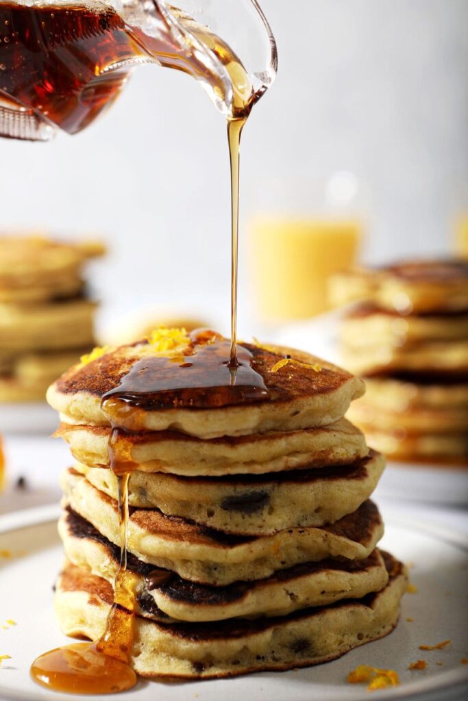 Maple syrup pours on top of a stack of homemade pancakes