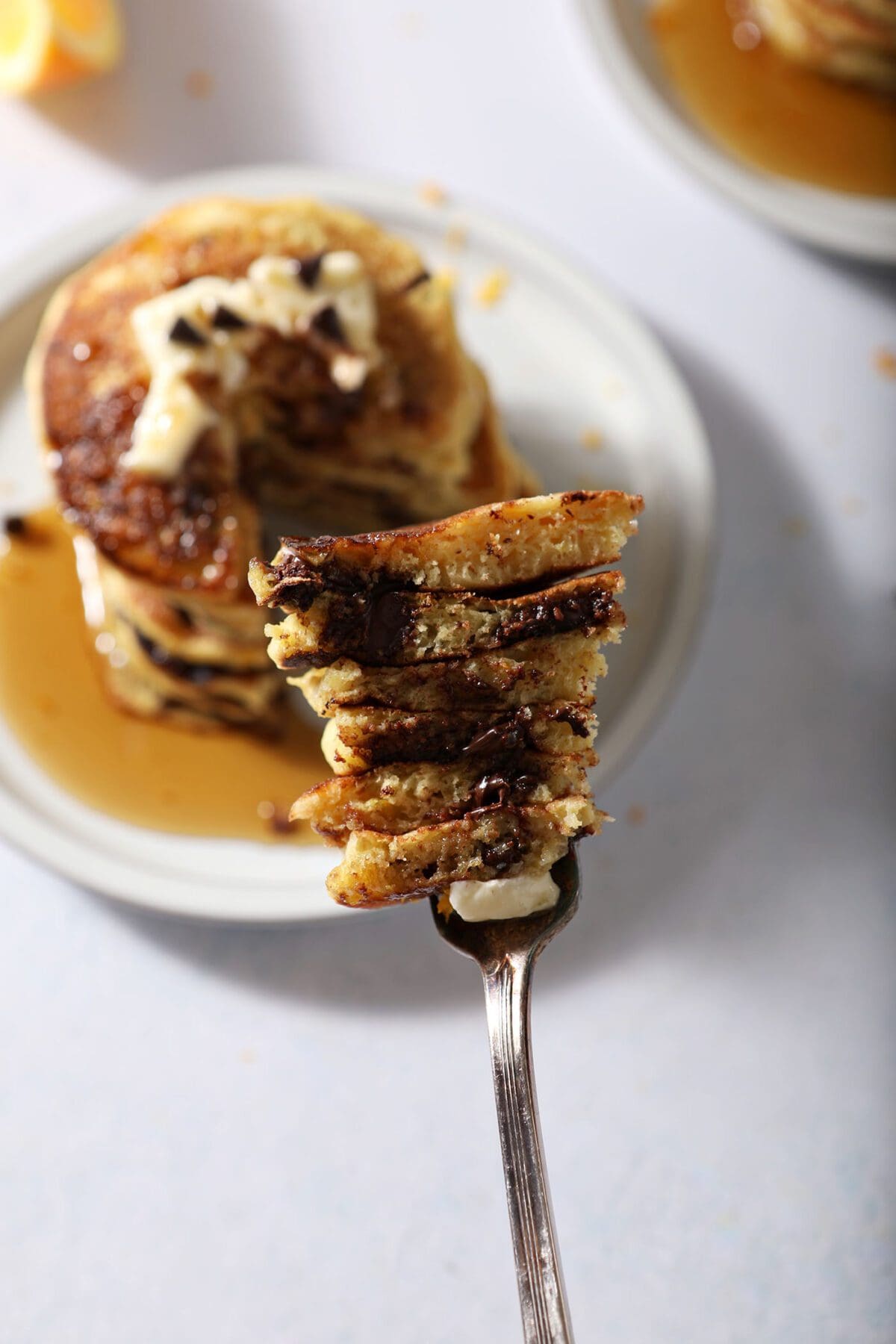 A fork holds a large bite of Orange Pancakes with Chocolate Chips above a plate