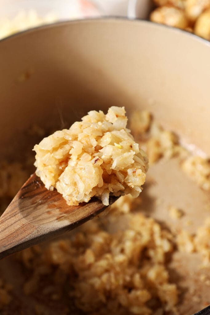 The cooked flour-veggie mixture on a wooden spoon above a Dutch oven