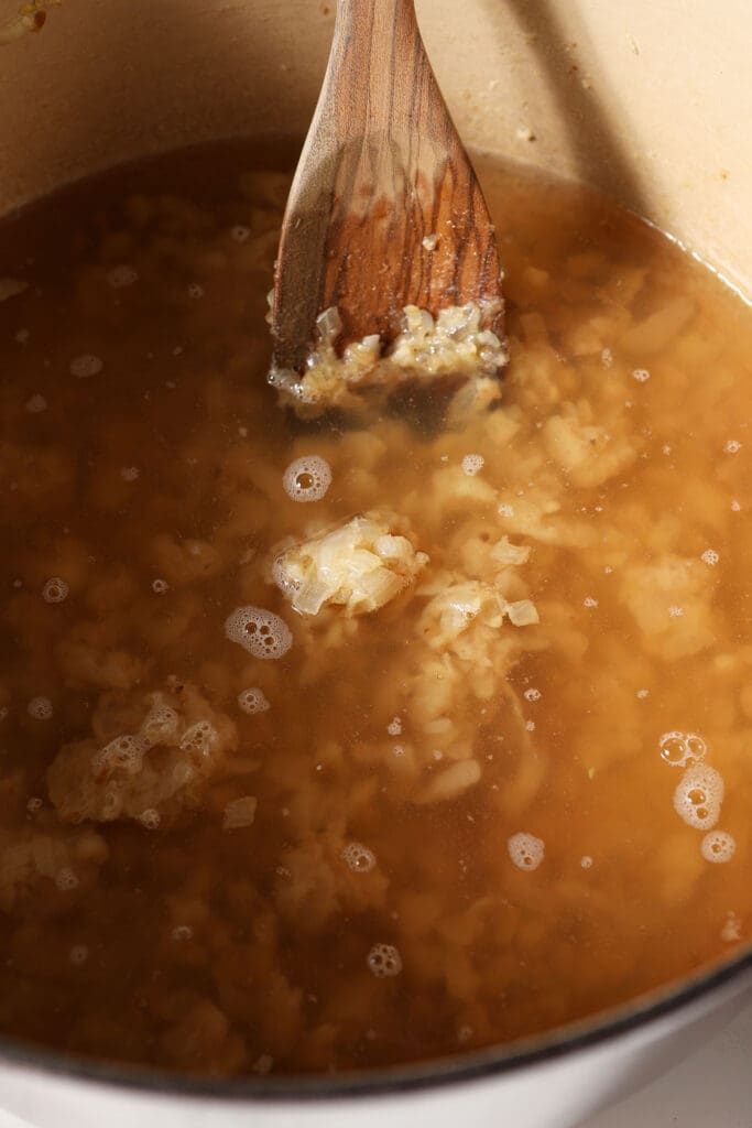 Broth in a dutch oven with veggies and a wooden spoon