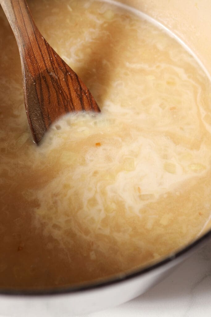 Half-and-half added to a Dutch oven of soup with a spoon in it