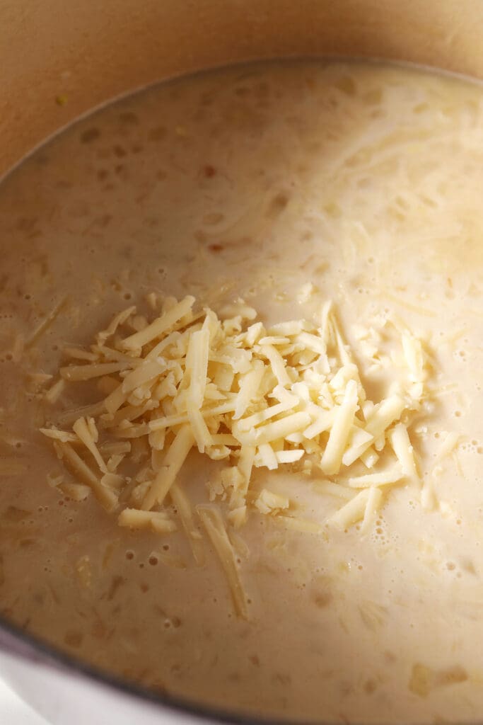 Shredded white cheese on top of soup in a Dutch oven