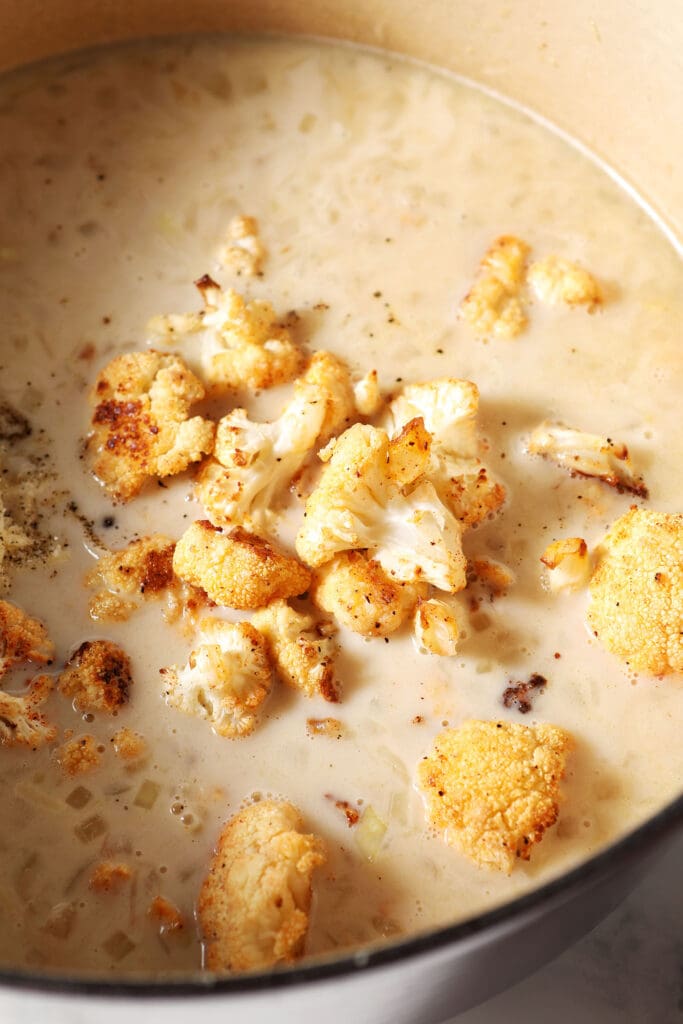 Roasted cauliflower florets on top of a white soup in a Dutch oven