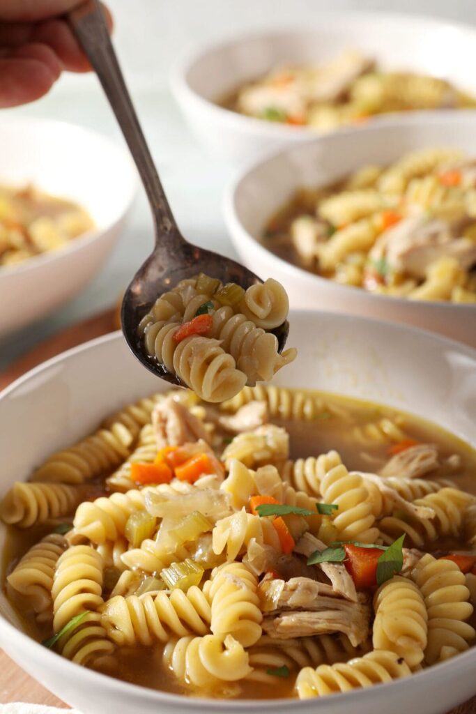 A spoon lifts a bite of Chicken Noodle Soup with Rotisserie Chicken out of a bowl