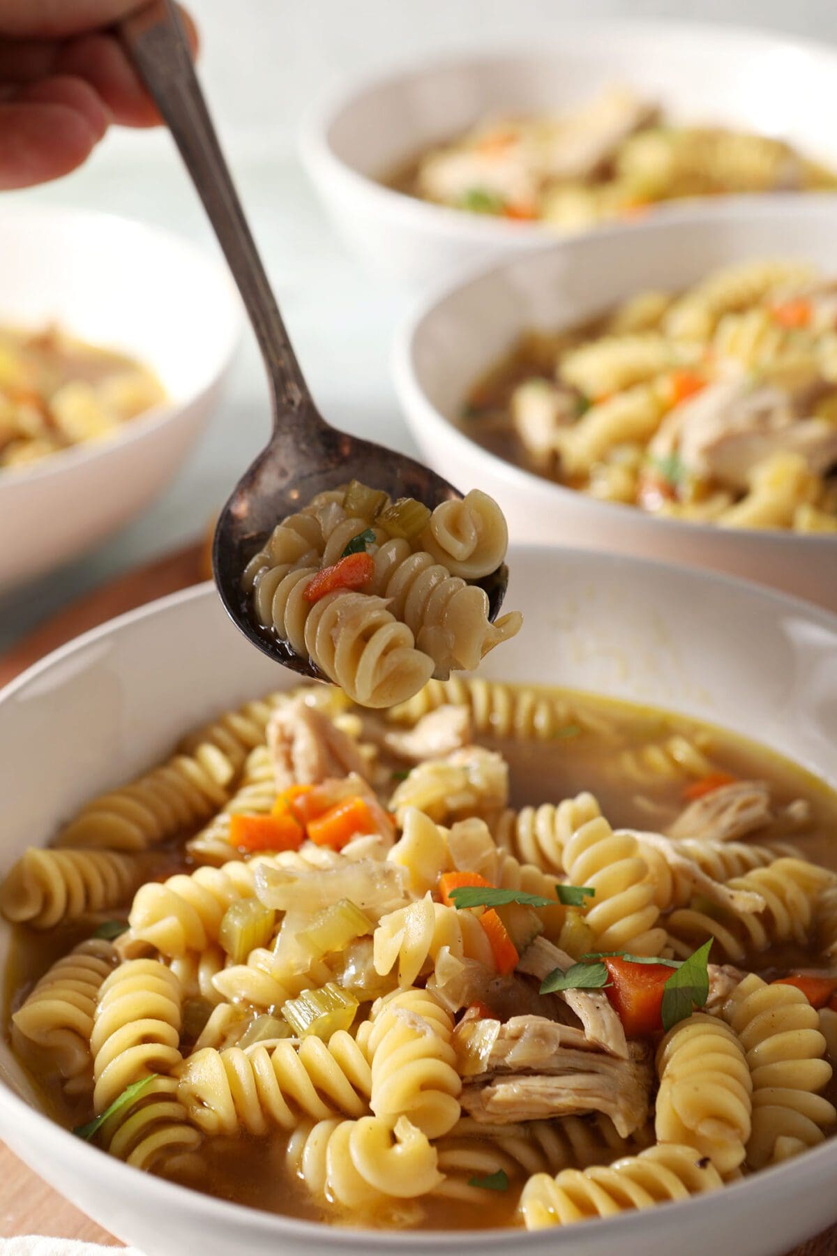 A spoon lifts a bite of Chicken Noodle Soup with Rotisserie Chicken out of a bowl