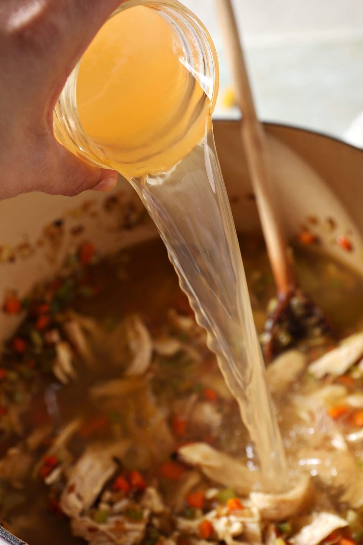 Chicken stock pours into a Dutch oven with chicken and veggies