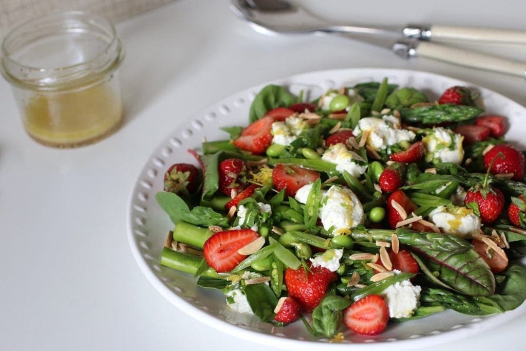 Bowl of salad next to glass jar of dressing on white table 