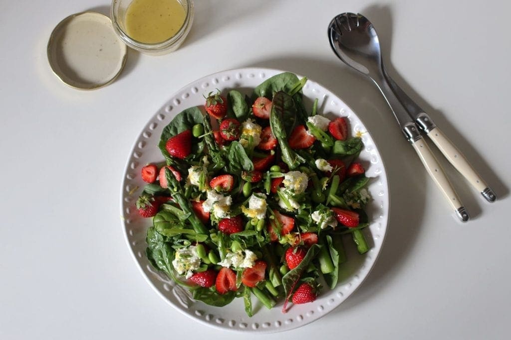 Overhead view of salad in a bowl next to utensils and jar of dressing 