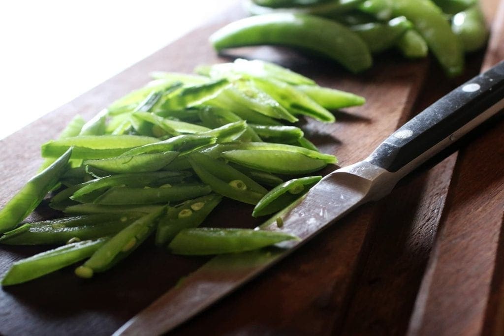 Sliced peas next to a knife on wooden cutting board 