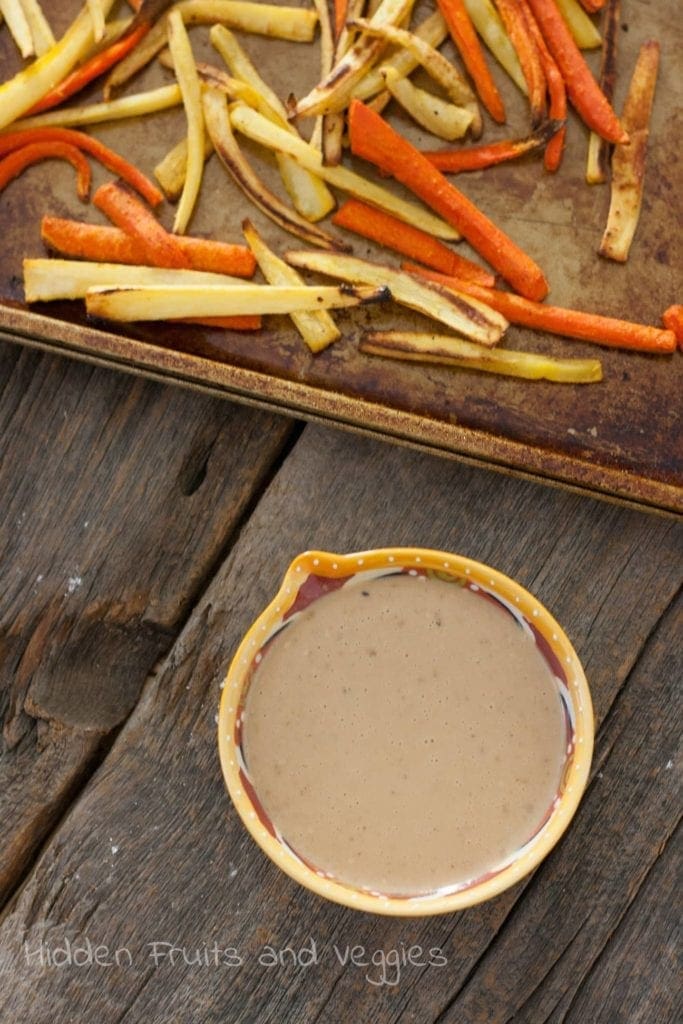 Parsnip fries on baking sheet next to dipping sauce 