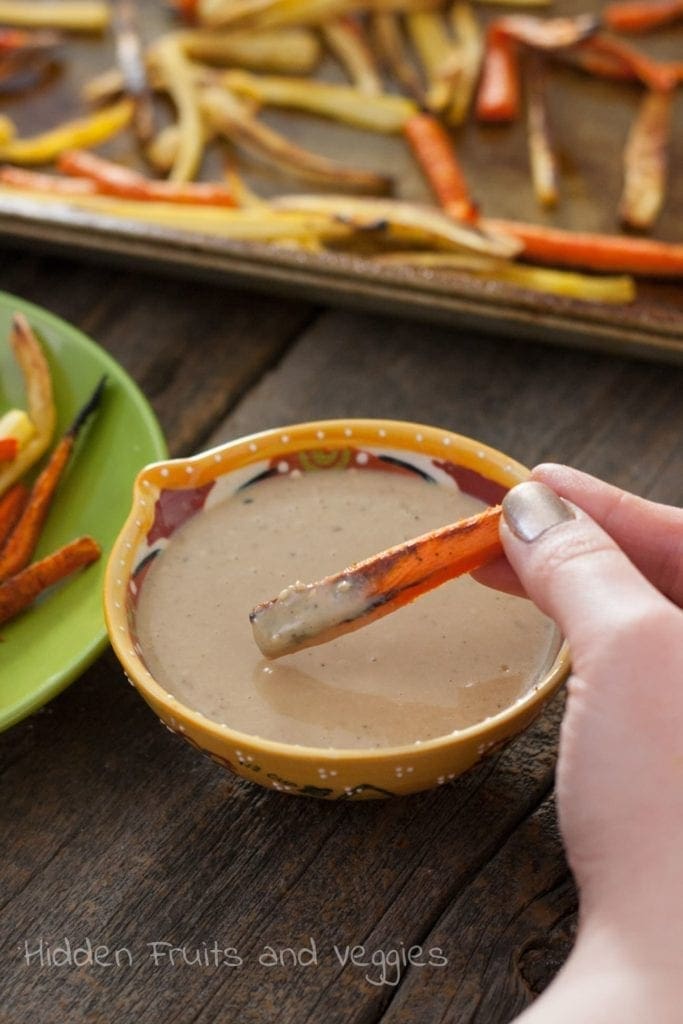 Hand dipping parsnip fry into dipping sauce 