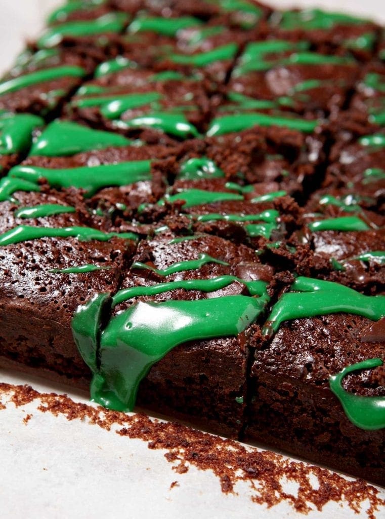 Close up of sliced brownies drizzled with green frosting in a pan