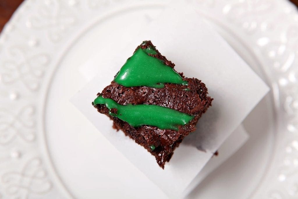 Close up of a single Guinness Brownie drizzled with green cream cheese frosting on a white plate