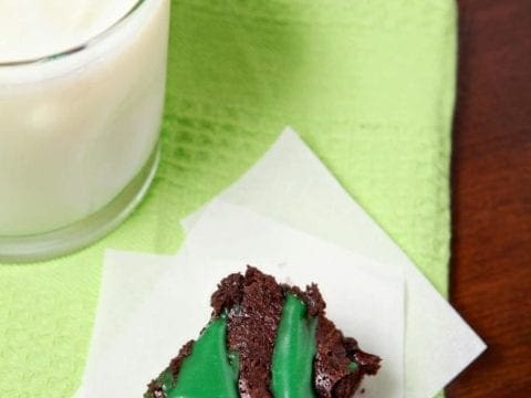 A Guinness Brownie with green frosting sits on a white napkin on top of a green towel next to a glass of milk