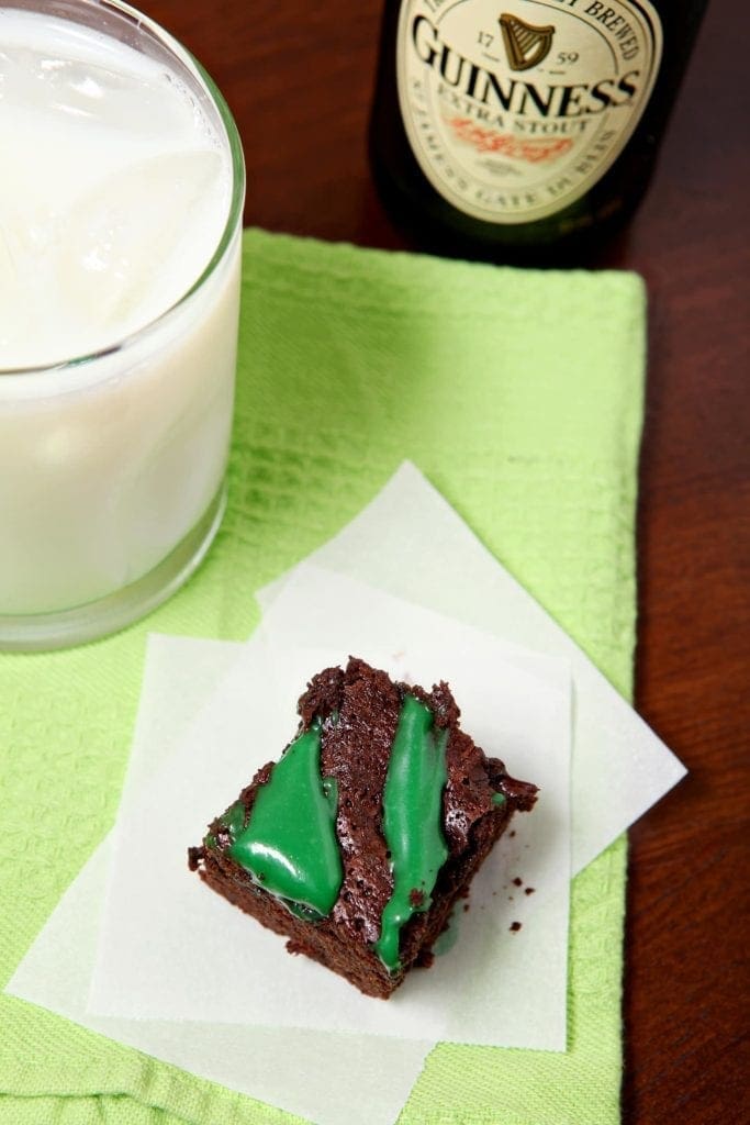 A Guinness Brownie with green frosting sits on a white napkin on top of a green towel next to a glass of milk