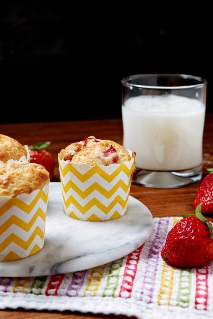 Muffins in yellow and white containers next to glass of milk