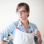 A woman wearing a white apron and glasses 