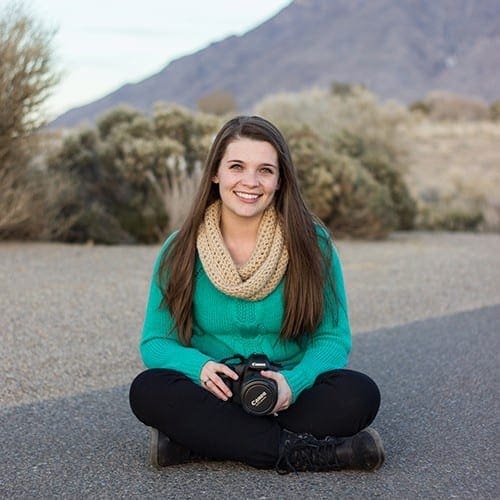 A woman sitting outside with a camera in front of a scenic view 