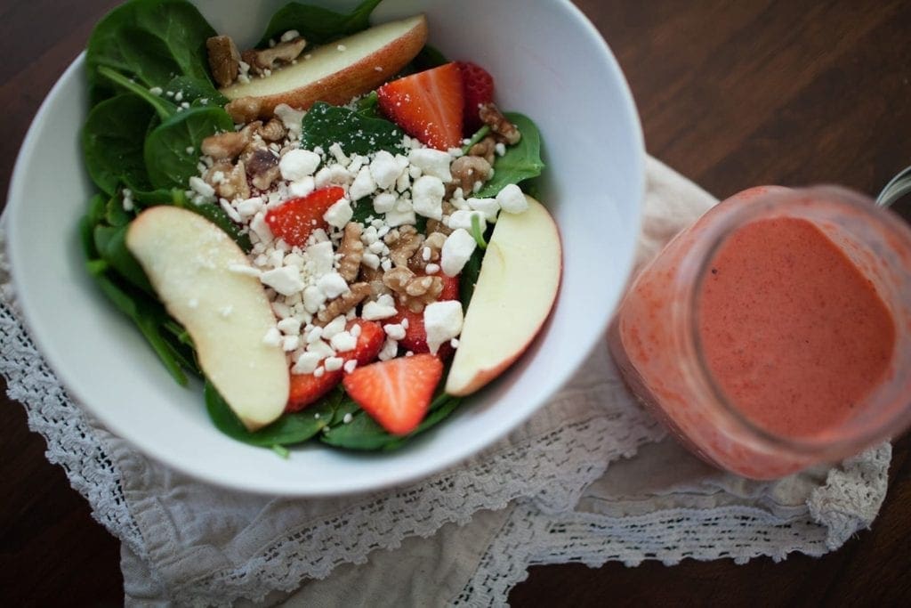 Overhead view of salad in a bowl on linens next to jar of dressing 