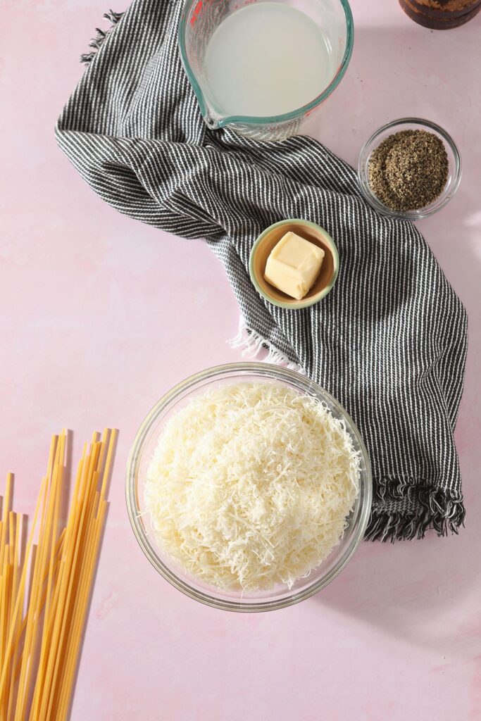 Pecorino romano with other pasta ingredients on a pink surface