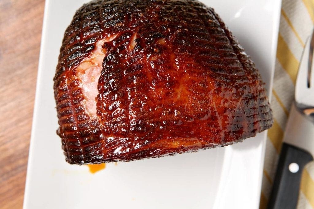 A whole glazed ham on a white platter, before slicing, from above