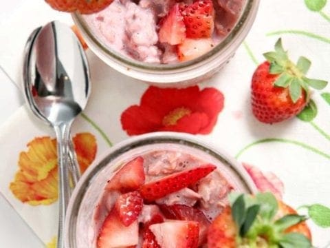 Two mason jars full of Strawberry Overnight Oats, topped with fresh strawberry slices before eating