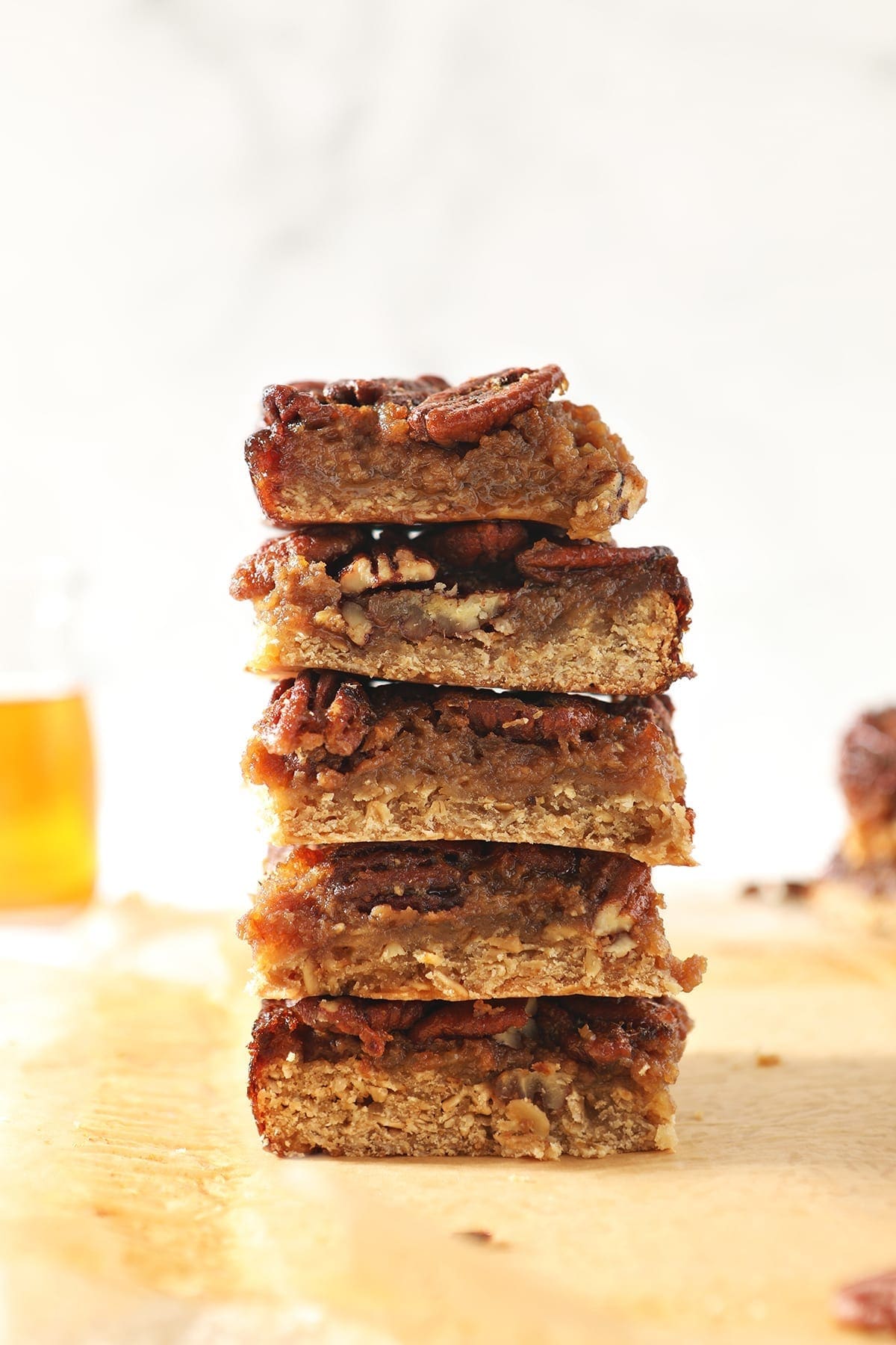 A stack of Bourbon Pecan Pie Bars in front of a vessel holding bourbon