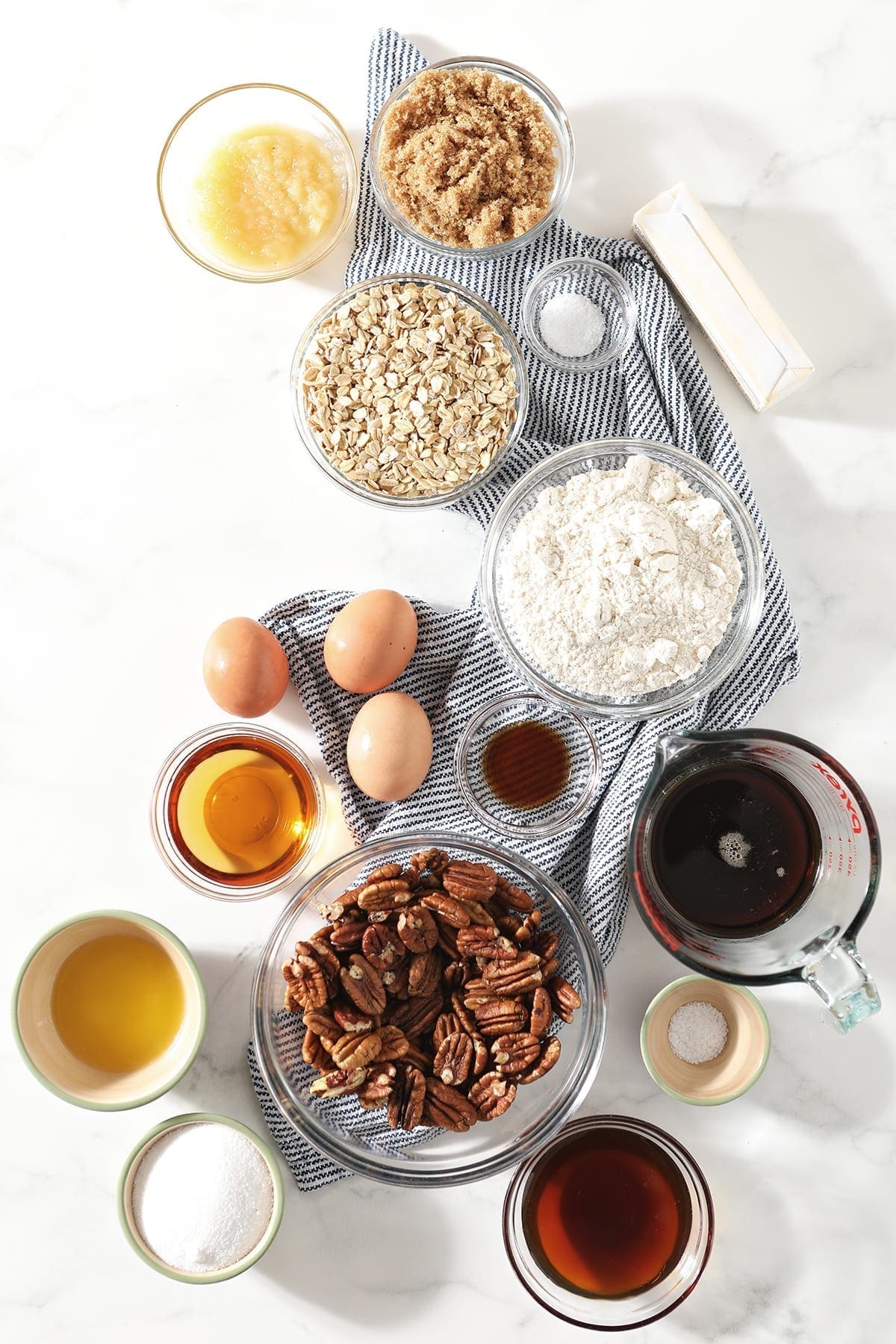 Ingredients to make Bourbon Pecan Pie Bars and their in bowls on top of a blue and white striped towel