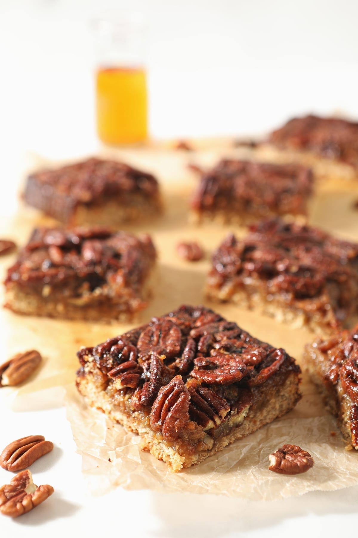 Sliced Bourbon Pecan Pie Bars sit on wax paper with a cup of bourbon behind them