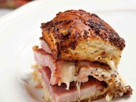 One Ham Goo Sandwich on a plate, with a platter of other sandwiches in the background, ready for eating