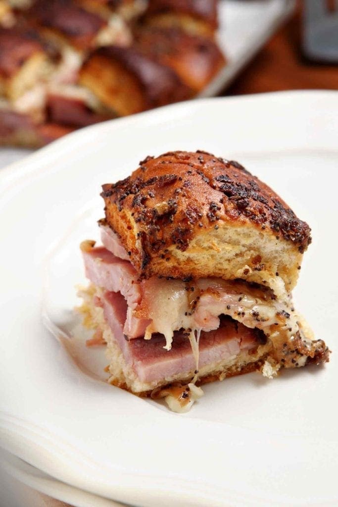 One Ham Goo Sandwich on a plate, with a platter of other sandwiches in the background, ready for eating