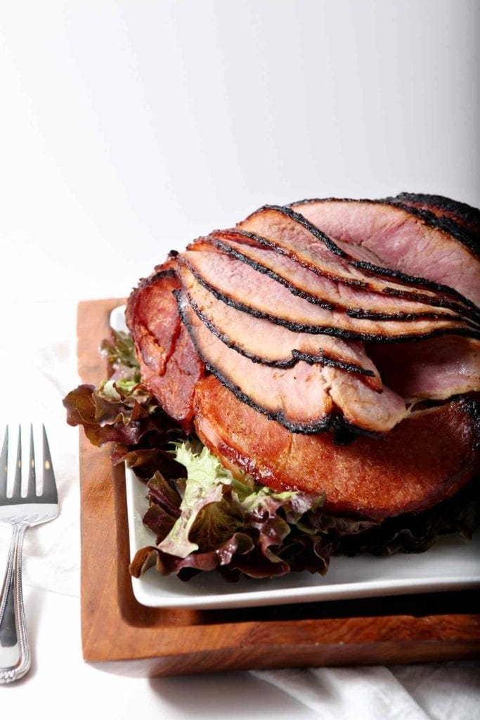 A homemade Honey Ham on a wooden platter, served on a white dish, ready for eating.