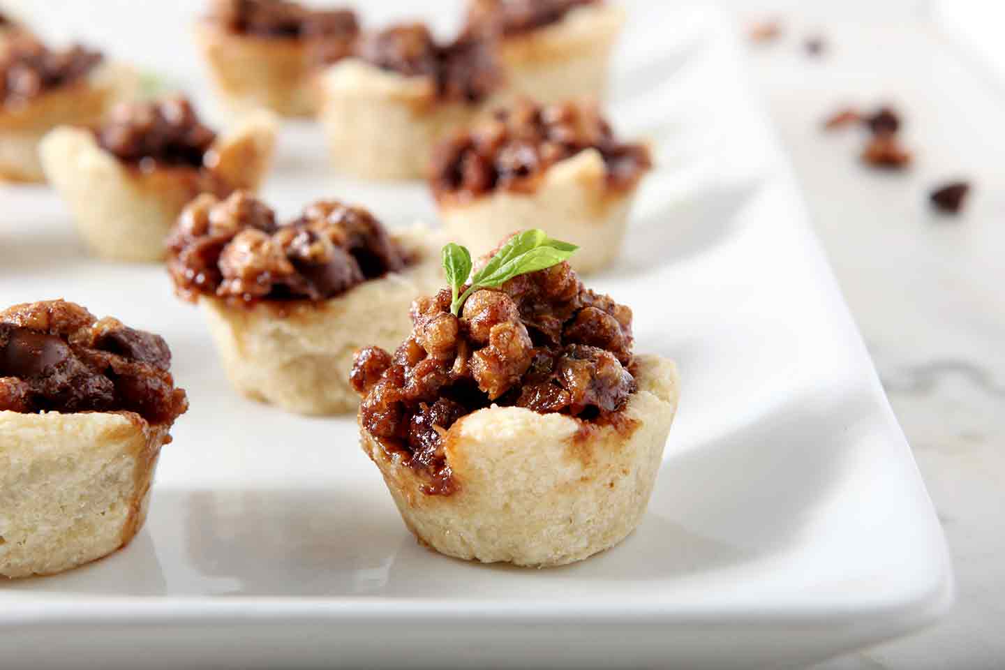 Mini Bourbon Chocolate Pecan Pies, after baking, on a white platter.